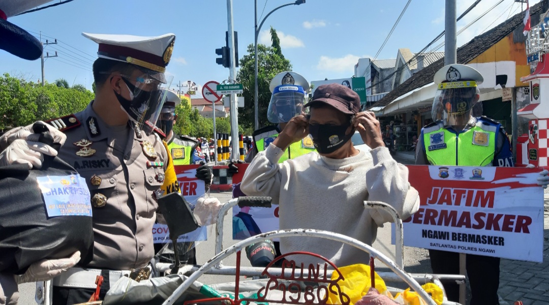 Kasat Lantas Polres Ngawi membagikan masker dan sembako ke tukang becak yang melintas di simpang Kartonyono. (Foto/Andik)