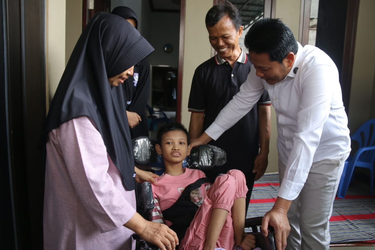 KURSI RODA - Mishelly Taliyata Zanih (16) gadis yang mengalami kelumpuhan sejak kecil, putri pasutri Sukandar dan Ny Kiswahyuni mendapat bantuan kursi roda yang diserahkan secara langsung oleh Bupati Sidoarjo, Subandi, Sabtu (15/11/2025).