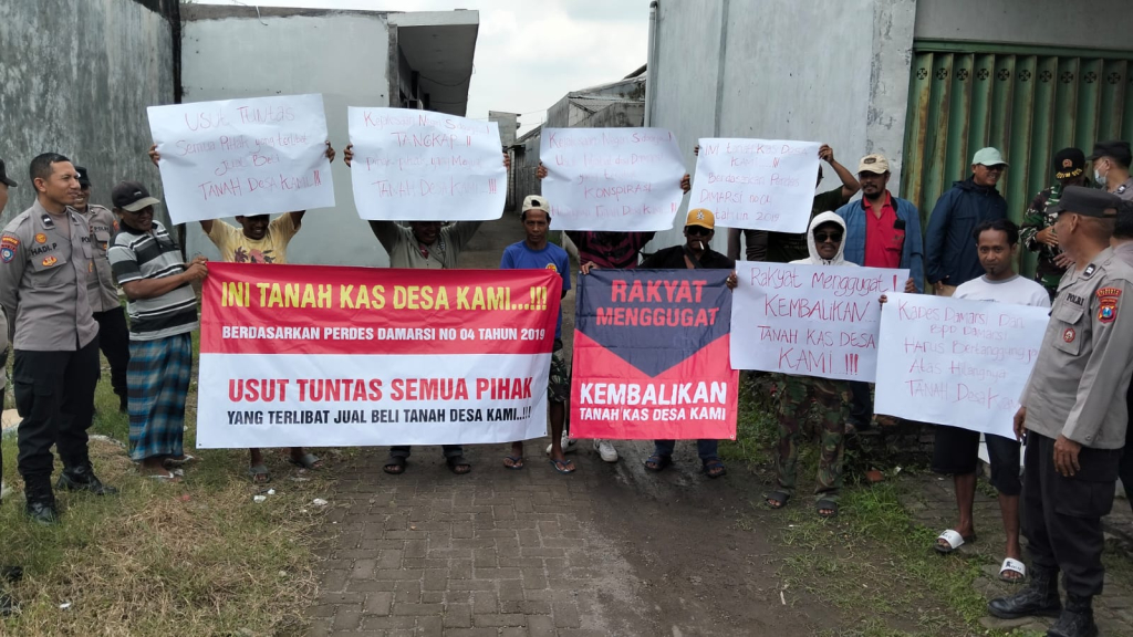 DEMO - Puluhan warga Desa Damarsi, Kecamatan Buduran, Sidoarjo demo di Tanah Kas Desa (TKD) yang dijadikan kos-kosan diantara dua perumahan dengan jumlah sebanyak 15 unit kos dengan membawa spanduk dan sound system, Selasa (17/02/2026).