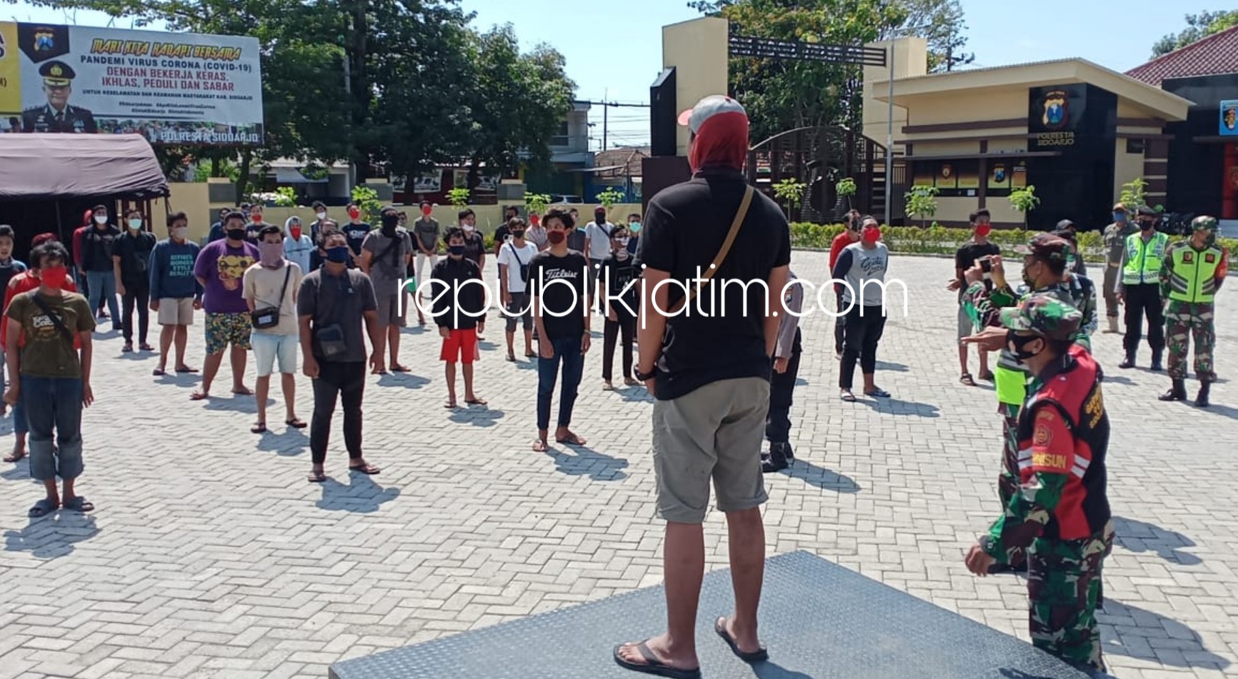 JALANI SANKSI - Ratusan pelanggar PSBB di Sidoarjo disanksi menyanyikan Bagimu Negeri, bersih-bersih dan mengenakan rompi pelanggaran di halaman Polresta Sidoarjo, Minggu (17/05/2020).