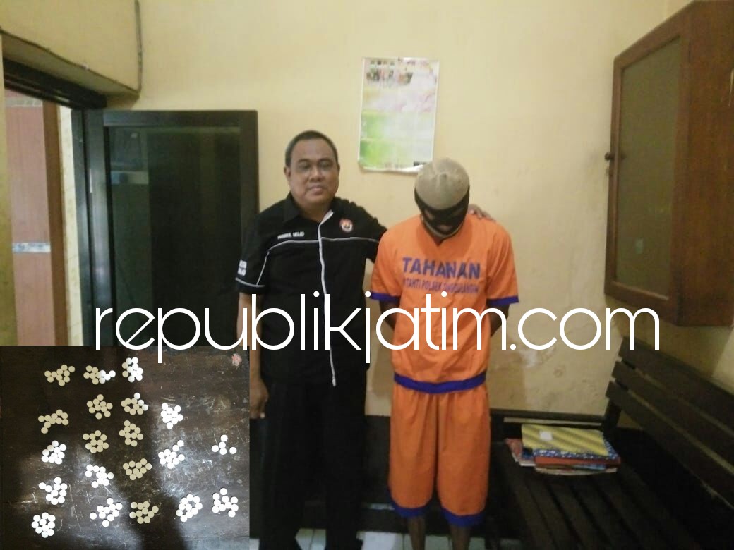 PENGEDAR - Tersangka pengedar pil koplo berlogo Y, Purnomo Hadi tertunduk lesu didampingi petugas Polsek Tanggulangin bersama barang bukti yang disita petugas, Selasa (22/05/2018).
