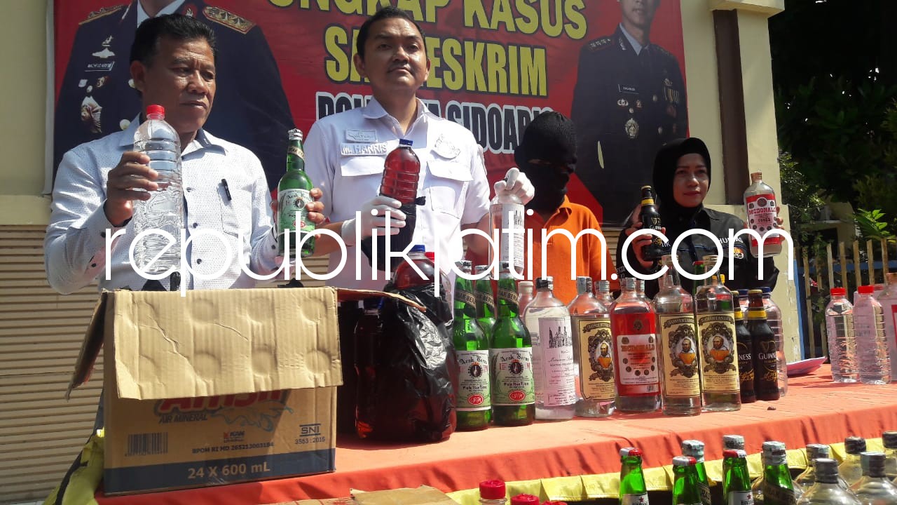 PRODUSEN - Kasat Reskrim, Polresta Sidoarjo, Kompol Muhammad Harris menunjukkan ratusan botol miras bermerek dan oplosan yang diamankan dari tersangka Punadi (50) beserta sejumlah lokasi lainnya, Selasa (05/06/2018).