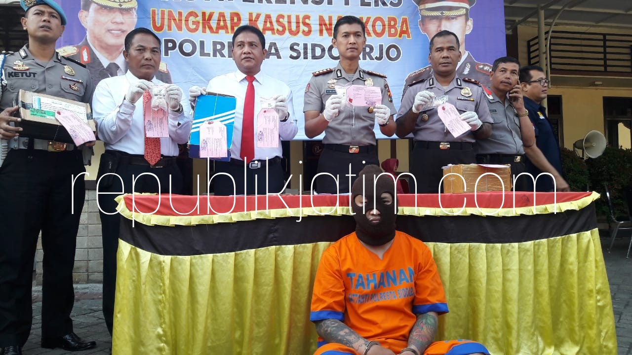 PENGEDAR - Tersangka pengedar sabu-sabu, Erfan Julianto (25) diamankan petugas Satuan Resnarkoba, Polresta Sidoarjo bersama barang buktinya 3,2 ons (320,22 gram) sabu-sabu yang hendak dipaketkan ke Bali, Sabtu (30/06/2018).