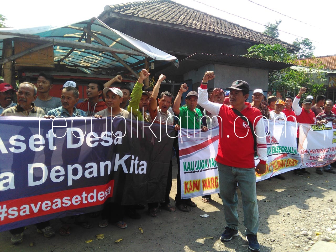 MENOLAK - Ratusan warga Desa/Kecamatan Krembung menggelar aksi membentangkan spanduk dan doa bersama menolak eksekusi lahan aset desa, Selasa (03/07/2018).
