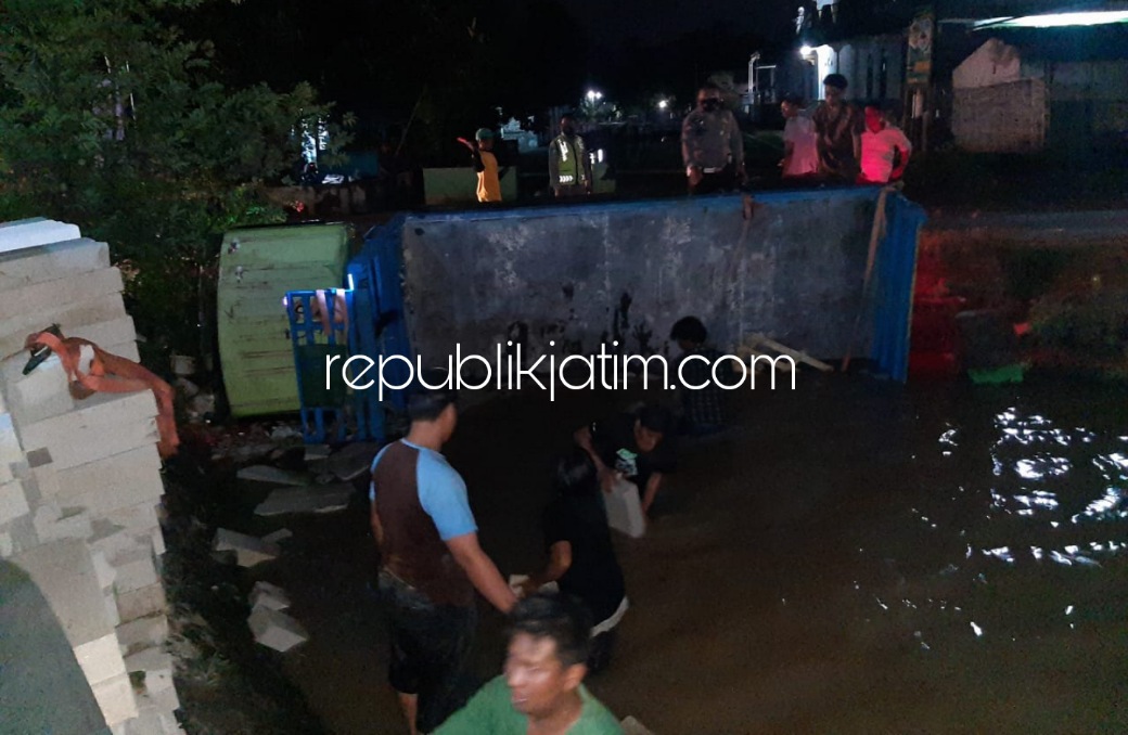 TERPEROSOK - Sejumlah warga membantu mengamankan dan mengevakuasi bata ringan yang truknya terperosok di Sungai PG Krembung bersama petugas kepolisian, Kamis (13/01/2022) malam.