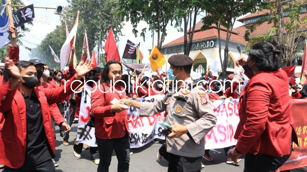 BAGI MASKER - Seorang perwira Polresta Sidoarjo tampak membagi masker untuk para peserta demo yang meluruk kantor DPRD Sidoarjo, Selasa (12/04/2022).