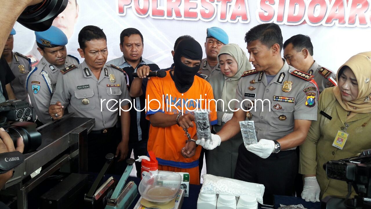 PRAKTEK - Tersangka Imam Muklison mempraktekkan cara pengepakan 5,3 juta butir pil PCC didampingi Kapolresta Sidoarjo, Kombes Pol Himawan Bayu Aji dan BPOM Surabaya serta Kadinkes Pemkab Sidoarjo di Polsek Wonoayu, Senin (22/01/2018).